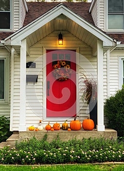 Bright red front door on a white house with a variety of pumpkins lined up on the porch.