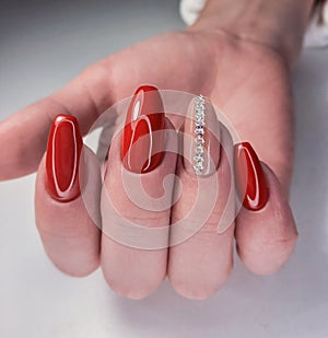 Bright red gel polish on long nails with beige design and stripes of rhinestones. An attractive manicure with a silver stripe desi