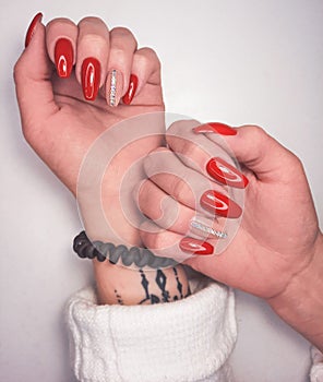 Bright red gel polish on long nails with beige design and stripes of rhinestones. An attractive manicure with a silver stripe desi