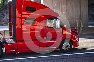 Bright red gorgeous big rig semi truck tractor transporting cargo running on the divided highway road going under the bridge