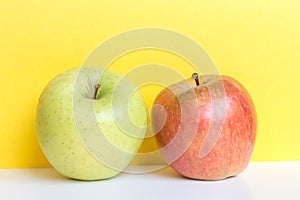 Bright red and green apples on yellow background and white table