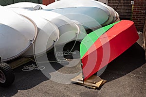 Bright red and green sailboat hull alongside stacked white fiberglass sailboat hulls