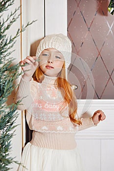 Bright red-haired little girl in a white hat and a beautiful dress is sitting in an autumn cafe. Redhead girl with big blue eyes