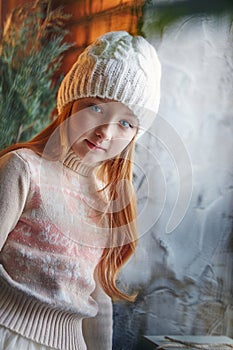 Bright red-haired little girl in a white hat and a beautiful dress is sitting in an autumn cafe. Redhead girl with big blue eyes