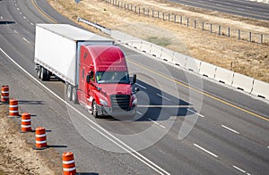 Bright red industrial big rig semi truck tractor transporting cargo in dry van semi trailer running on the divided highway road
