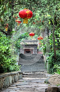 Bright red lanterns hang over a smooth stone path leading to steps up to a temple at the Summer Palace in China