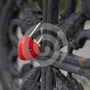 Bright red lock in the shape of a heart on a black old railing of the bridge, love symbol