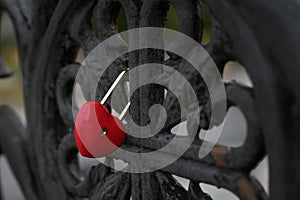 Bright red locked padlock in the shape of a heart on a black old railing of the bridge, love symbol