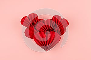 Bright red paper heart of many hearts of asian ribbed fans on pastel pink background, top view, copy space. Valentine day, wedding