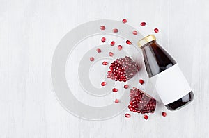 Bright red pomegranate juice in glass bottle with blank label, sliced fruit on white wooden board, top view, copy space, template.