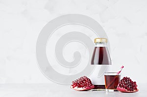 Bright red pomegranate juice in glass bottle mock up with blank label, straw, wine glass, fruit grains on white wood table.