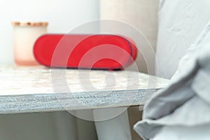 Red radio alarm clock and candle jar on a bedside table nightstand, with bed and linens showing in soft colors photo