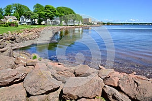 Bright red rocks forming barrier along Charlottetown Harbour with reflections on water surface