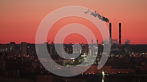 Bright red sky at sunrise on the background of a sleeping city and a factory. Smoking factory chimneys on the background