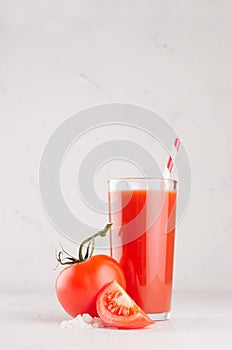 Bright red tomato cocktail in elegance glass with glossy tomatoes, salt, straw and ripe piece on white wooden board, vertical.