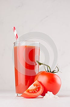 Bright red tomato cocktail in elegance glass with glossy tomatoes, salt, straw and ripe piece on white wooden board, vertical.