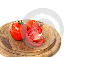 A bright red tomato, cut in half, is placed on a wooden cutting board. on a white background.