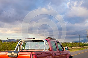 Bright red truck driving by. Beautiful cloudy sky and grassy field in background.