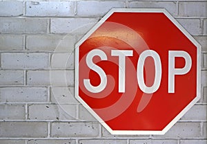 A bright red and white stop sign bolted to white brick wall