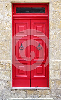 Bright red wooden door of a house with black doorknob rings