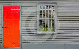 Bright red wooden door with nail decoration and multiple paned window in wall of colonial building