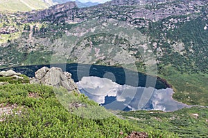 Bright reflection of white clouds and blue sky in water of a mountain lake. Summer landscape in Ergaki nature park