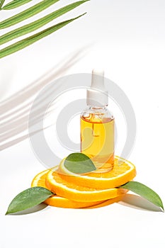 A bright and refreshing display of a Vitamin C serum bottle on a podium made of fresh orange slices and green leaves.