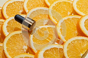 A bright and refreshing display of a Vitamin C serum pipette alongside fresh orange slices on orange background