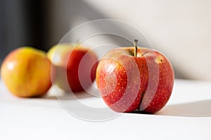 Bright ripe apple of an unusual shape buttocks in the light of the sun on a white background with ordinary apples behind. photo