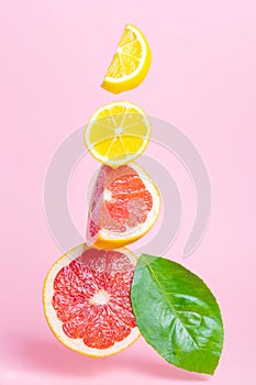 Bright ripe juicy sliced lemon and grapefruit hang in the air on a pastel pink background.