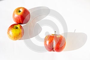 Bright ripe red apple of an unusual shape of an ass in the light of the sun on a white background with two usual apples