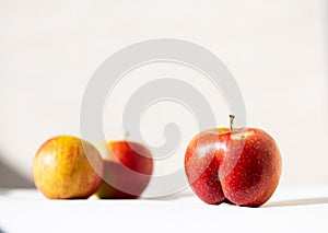 Bright ripe red apple of an unusual shape in the shape of an ass in the light of the sun on a white background with two usual appl