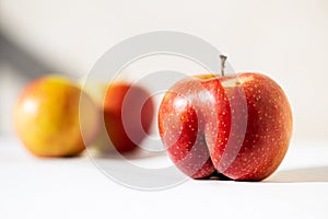 Bright ripe red apple of an unusual shape in the shape of an ass in the sunloght on a white background with two usual apples. photo
