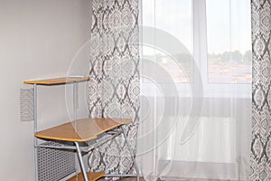 Bright room with a curtained window, a computer desk near a gray wall. The interior of a small room