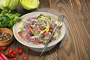 Bright salad of purple cabbage, white cabbage, bell pepper in a plate on a wooden table. Fresh vegetable salad. Food background.