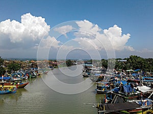 A bright scenery, blue sky, clouds, and a ship at the Ujung Negoro Beach pier in Central Java, Indonesia.