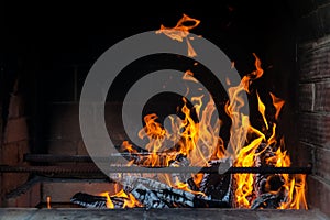 Bright sharp thin tongues of orange, yellow and red flames on a dark background in a brick oven behind metal rods, heating the