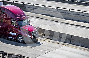 Bright shiny big rig purple semi truck transporting cargo in semi trailer moving on the divided highway intersection with concrete