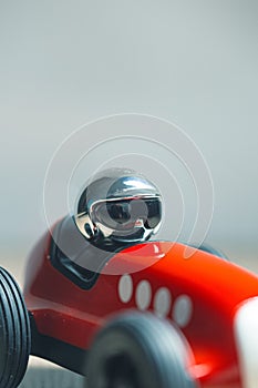 Bright silver helmet on a racing driver on a red toy vintage racing car