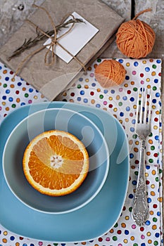 Bright sliced orange lies on two plates. Nearby is a fork, an old notepad and a few tangles of orange thread for knitting.