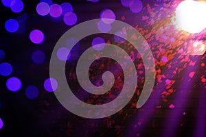 Bright spotlight, beams of light and falling confetti in darkness of night club, bokeh effect