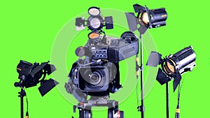 Bright spotlights stand near professional video camera on a green screen.