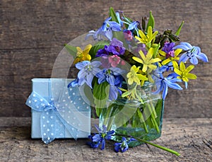 Bright spring flowers bouquet in a glass vase and gift box on old wooden background. Mother`s Day,Birthday,Women`s Day greeting ca