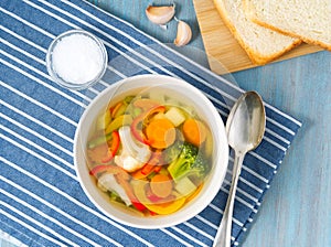 Bright spring vegetable soup with cauliflower, broccoli, pepper, carrot, green peas. Top view, blue wooden background.