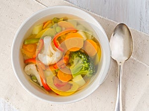 Bright spring vegetable soup with cauliflower, broccoli, pepper, carrot, green peas. Top view, white wooden background.