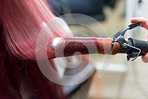 Bright strand of long hair with modulations from crimson to red curled on a curling iron