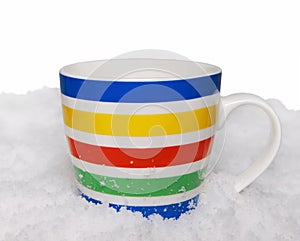 Bright striped mug stands in the snow on a white background