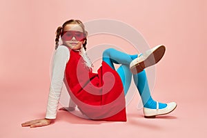 Bright style. Beautiful little girl, child in red dress, blue tights and red glasses posing over pink studio background