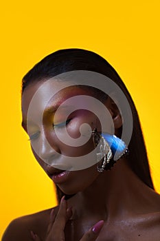 Bright stylish black woman on a yellow background with a blue butterfly on her face.