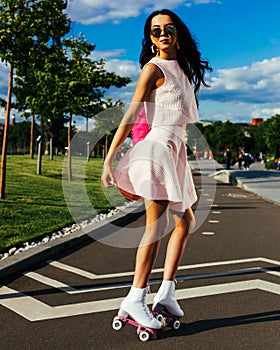 Bright summer portrait of an asian girl in a summer bright outfit and sunglasses with a pink backpack on roller skates